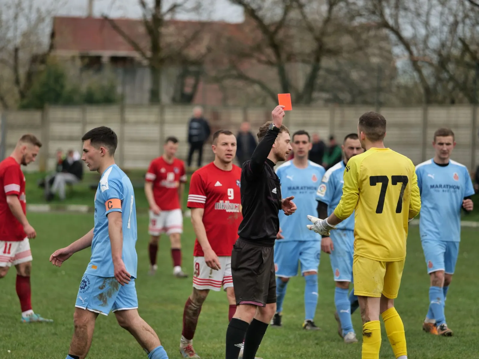 A heated moment as a referee shows a red card to a goalkeeper during a competitive soccer match.